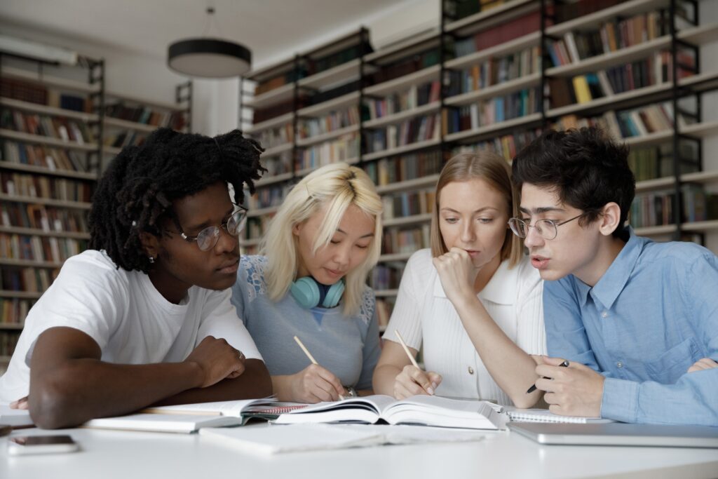 Four students huddled around a table in a school library.